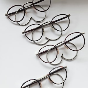 May include: Four pairs of eyeglasses arranged in a diagonal line. Each pair features round, dark brown tortoiseshell-patterned rims with silver-toned metal bridges and temples. The frames include integrated nose pads and curved ear pieces.