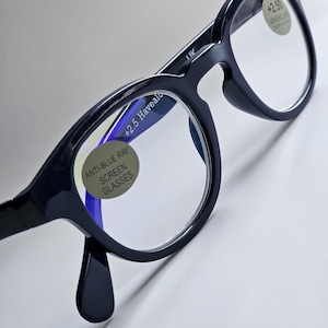 May include: Black-framed glasses with clear lenses featuring anti-blue ray screen protection. The lenses have circular stickers indicating +2.5 magnification and the text Anti-Blue Ray Screen Glasses. The frames have a glossy finish and bridge.