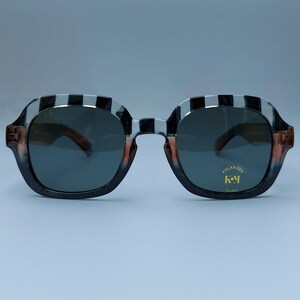 Może przedstawiać: Okulary przeciwsłoneczne w czarno-biały wz&oacute;r z polaryzacyjnymi szkłami. Okulary mają złotą etykietę z napisem "POLARIZED" i "key" złotą czcionką.