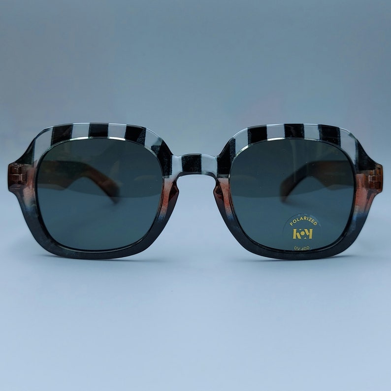 Może przedstawiać: Okulary przeciwsłoneczne w czarno-biały wz&oacute;r z polaryzacyjnymi szkłami. Okulary mają złotą etykietę z napisem "POLARIZED" i "key" złotą czcionką.