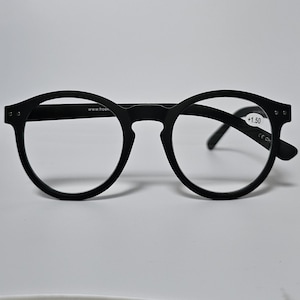 May include: Matte black round-frame reading glasses with a keyhole bridge. The right lens features a small white sticker with the text +1.50. The inner temple arm displays the text www.hoek and the other arm shows CE CH.