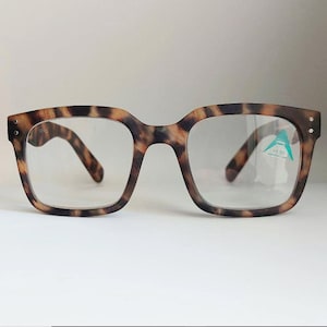 May include: Tortoiseshell reading glasses with a +1.50 magnification. The glasses have a square frame with clear lenses.