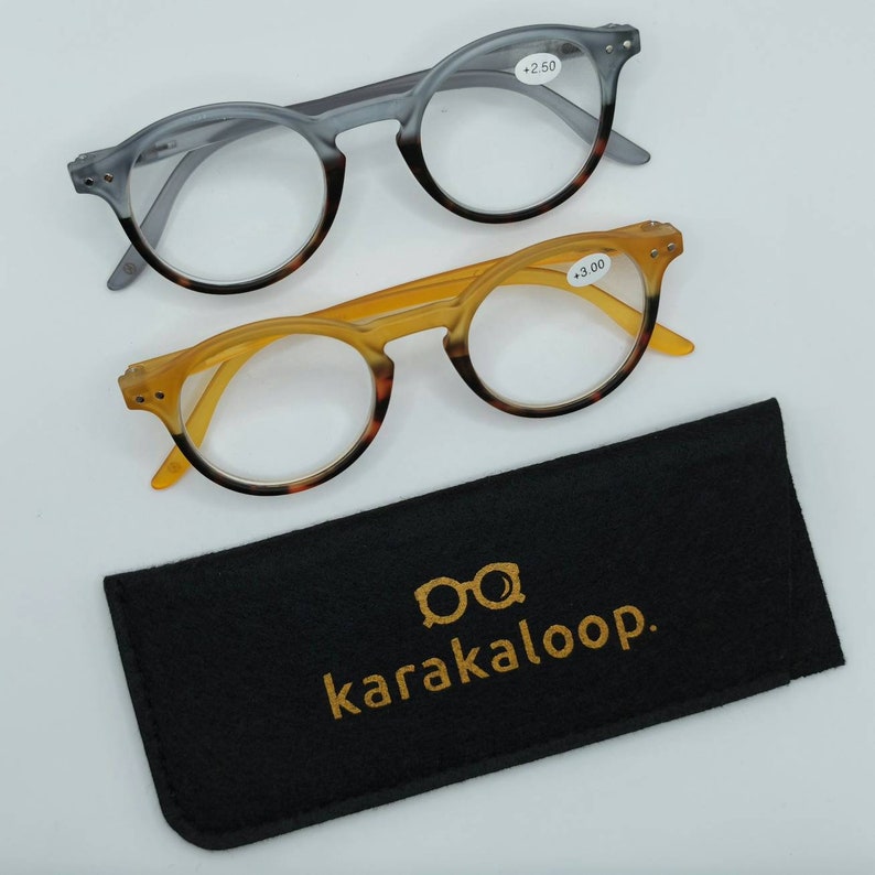 Op de afbeelding: Twee paar ronde leesbrillen met schildpadranden en heldere glazen. De brillen zitten in een zwarte wollen etui met de tekst "karakaloop." in goud gedrukt. De brillen hebben een vergroting van +2,50 en +3,00.
