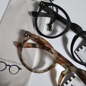 May include: Two pairs of spectacles with clear lenses. One has a black frame, the other a brown and tan tortoiseshell pattern. A light-coloured drawstring bag and small tags are also visible.
