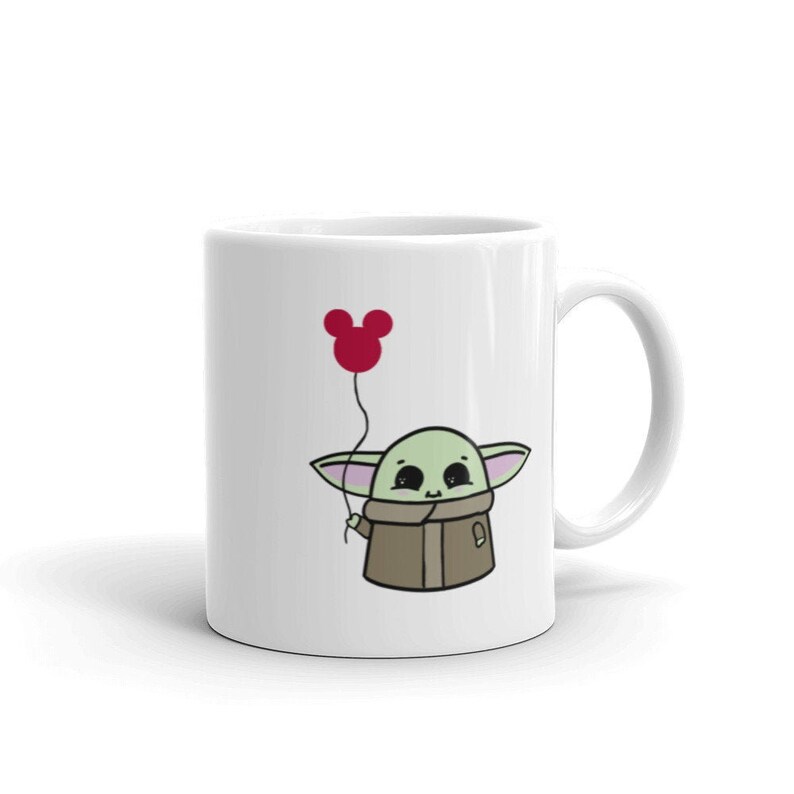 May include: White ceramic mug with a cartoon illustration of a green character holding a red balloon shaped like a Mickey Mouse head.
