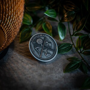 May include: A silver-toned metal pin with the words "Carpe Diem" inscribed around the edge. The pin features a tree, a rose, a scythe, and an hourglass.