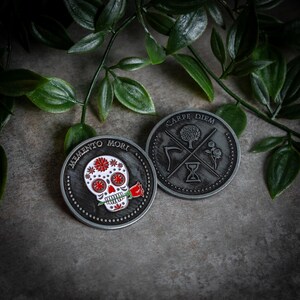 May include: Two silver-toned coins with black and white designs. The first coin features a sugar skull with a red rose in its mouth and the text "Memento Mori". The second coin features a tree, an hourglass, and a scythe with the text "Carpe Diem".