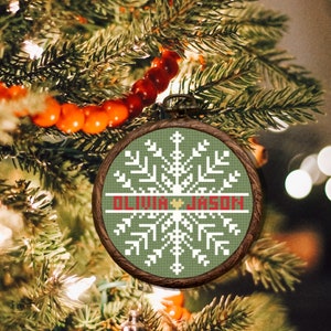 May include: A green and white cross-stitch ornament with a snowflake design and the names "Olivia" and "Jason" in red.