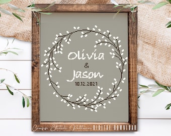 Puede incluir: Un patrón de punto de cruz con una corona de flores blancas y ramas marrones con el texto "Olivia & Jason 10.12.2021" en una fuente marrón sobre un fondo gris.