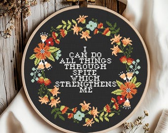 Puede incluir: Un bastidor de bordado de punto de cruz con fondo negro y diseño de corona floral. El texto dice "I CAN DO ALL THINGS THROUGH SPITE WHICH STRENGTHENS ME". La corona floral incluye flores naranjas, rojas y azules.