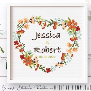 May include: Cross stitch pattern featuring a heart-shaped floral wreath with the names Jessica & Robert and the date 06.12.2022.