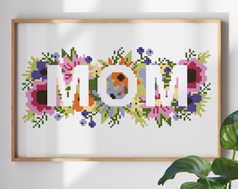 Puede incluir: Patrón de punto de cruz con la palabra "MOM" rodeada de flores coloridas. Las letras son blancas y las flores son en tonos de rosa, morado, azul, verde, naranja y amarillo.