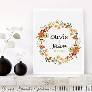 Puede incluir: Patr&oacute;n de punto de cruz con una corona de flores con los nombres Olivia & Jason y la fecha 10.12.2022. La corona es en tonos de naranja, rojo, verde y azul.