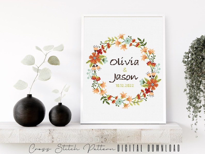 Puede incluir: Patr&oacute;n de punto de cruz con una corona de flores con los nombres Olivia & Jason y la fecha 10.12.2022. La corona es en tonos de naranja, rojo, verde y azul.