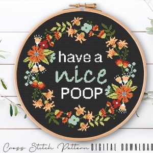Può includere: Uno schema di punto croce in bianco e nero con una ghirlanda di fiori che circonda il testo "have a nice POOP".