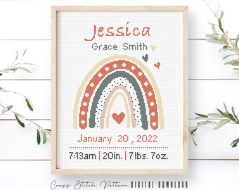 May include: A cross stitch pattern featuring a rainbow with a heart in the center. The rainbow is in shades of orange, green, and pink with white polka dots. The text "Jessica Grace Smith" is above the rainbow, and the text "January 20, 2022 7:13am | 20in. | 7 lbs. 7oz." is below the rainbow.