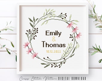Può includere: Schema di punto croce con una ghirlanda floreale con fiori rosa e foglie verdi. Il testo "Emily & Thomas 10.12.2022" è all'interno della ghirlanda.