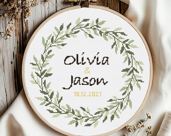 Puede incluir: Un patrón de punto de cruz con una corona de hojas verdes con los nombres Olivia & Jason y la fecha 10.12.2021 en el centro.