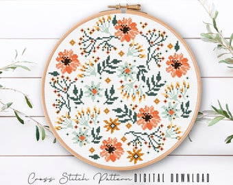 May include: A cross stitch pattern featuring a circular design of orange, yellow, and green flowers on a white background. The pattern is displayed in a wooden embroidery hoop.
