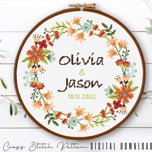 Puede incluir: Patr&oacute;n de punto de cruz con un dise&ntilde;o de corona de flores. La corona est&aacute; en tonos de naranja, rojo, verde y azul. El texto en el centro dice "Olivia & Jason 10.12.2022".