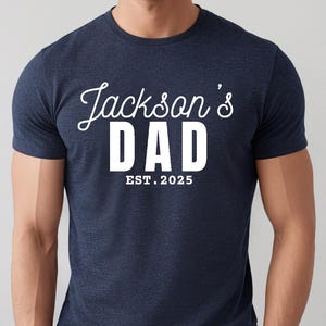 May include: A heather navy blue t-shirt with white text that reads "Jackson's Dad Est. 2025".