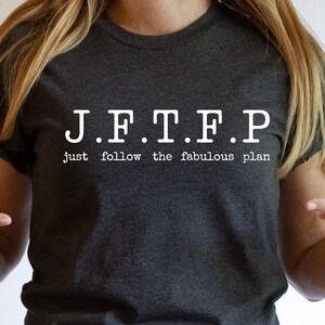 May include: Dark heather grey t-shirt with white text that reads "J.F.T.F.P. Just follow the fabulous plan."