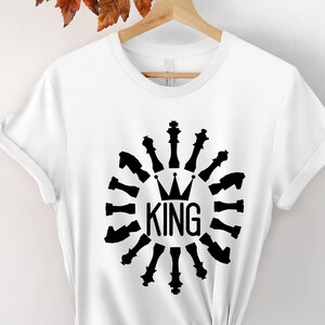 Peut inclure: T-shirt blanc avec un motif noir représentant un roi des échecs entouré de pièces d'échecs. Le motif indique "KING" avec une couronne au-dessus du mot.