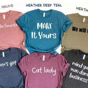 May include: Six different t-shirts with various sayings printed on them. The shirts are in different colors, including heather mauve, heather deep teal, heather olive, heather navy, heather maroon, and dark grey heather.