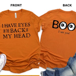 May include: Orange t-shirt with the text "I have eyes in the back of my head" on the front and "Boo! I see you!" with two cartoon eyes on the back. The shirt is heather autumn color.