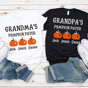 May include: Two white t-shirts with black text that reads "Grandma's Pumpkin Patch" and "Grandpa's Pumpkin Patch". Each shirt has three orange pumpkins with hearts on them and the names "Jack", "Jamie", and "Emma" underneath. The shirts are laid out on a light wood surface with a pair of white sneakers and blue jeans.