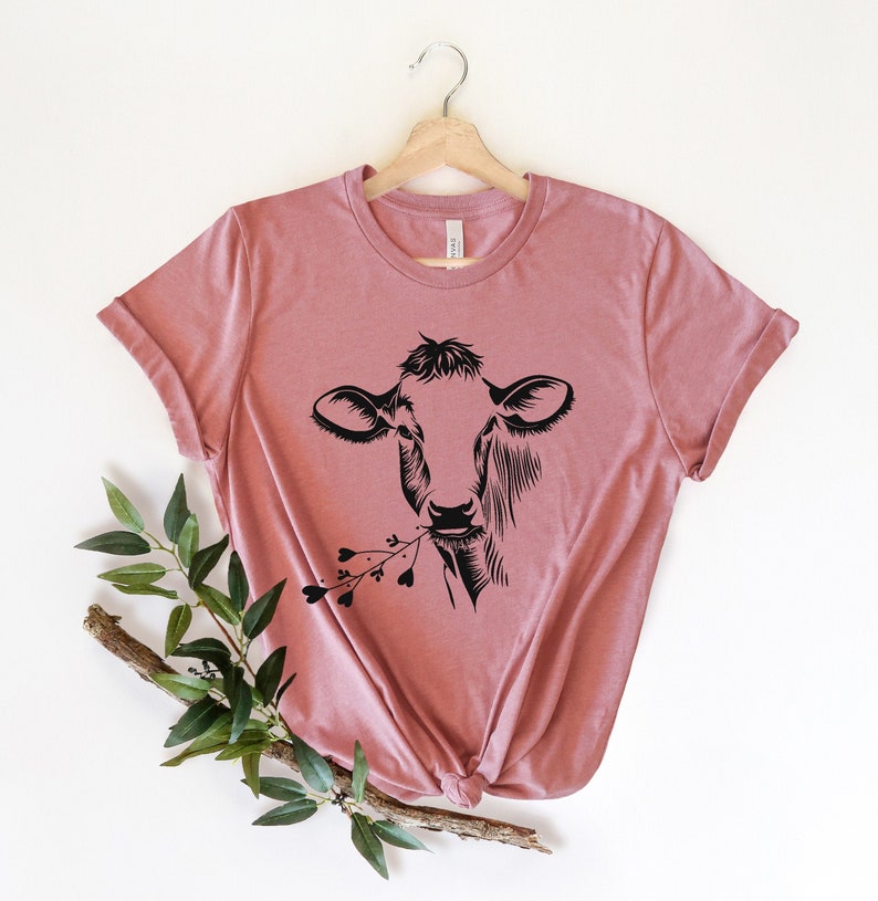 May include: A dusty rose t-shirt with a black silhouette of a cow with flowers in its mouth.
