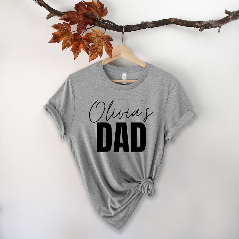 May include: Gray t-shirt with black text that reads "Olivia's Dad".