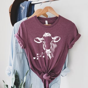 May include: A maroon t-shirt with a white silhouette of a cow's head with flowers in its mouth.