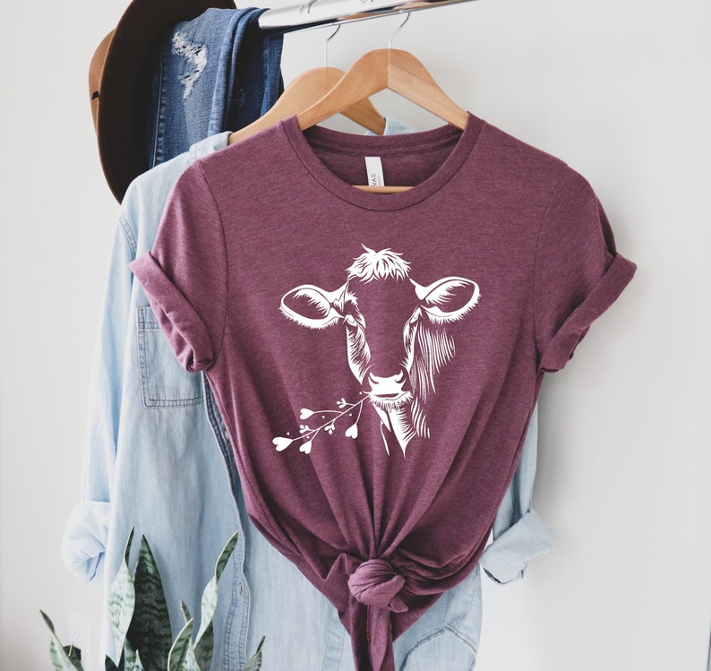 May include: A maroon t-shirt with a white silhouette of a cow's head with flowers in its mouth.