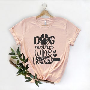 May include: A light pink t-shirt with a black graphic that says "Dog mother wine lover" with a paw print and a wine bottle graphic.