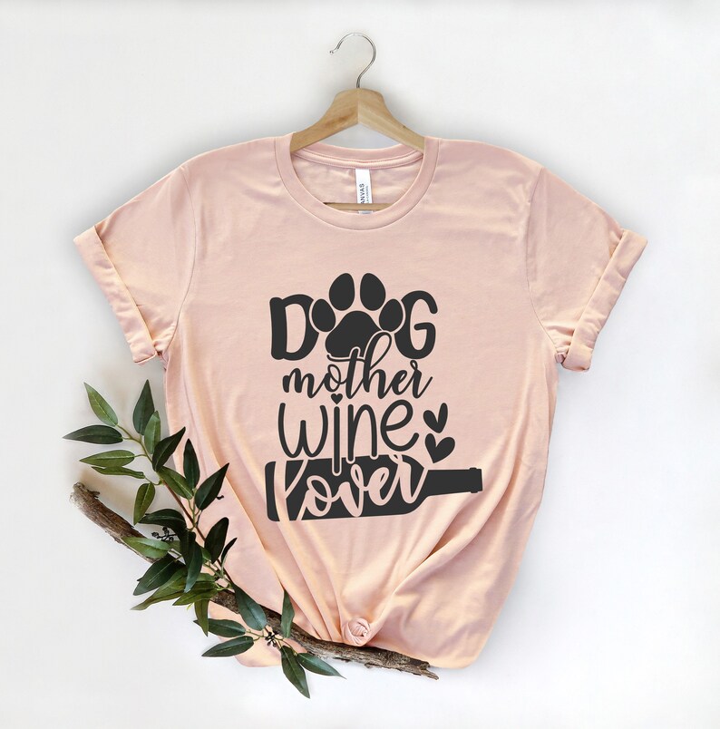 May include: A light pink t-shirt with a black graphic that says "Dog mother wine lover" with a paw print and a wine bottle graphic.
