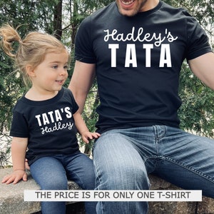 May include: Black t-shirts with white text. One shirt reads "Hadley's TATA" and the other reads "TATA'S Hadley". The shirts are worn by a child and an adult. The text "THE PRICE IS FOR ONLY ONE T-SHIRT" is at the bottom.