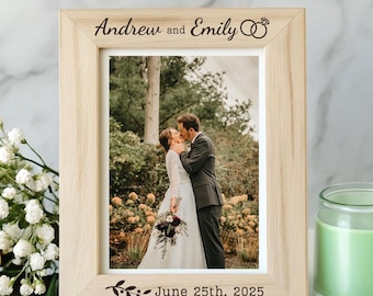 May include: A light-colored wooden picture frame with a wedding photo of a couple kissing. The frame is engraved with "Andrew and Emily" and the date "June 25th, 2025". A yellow rose and a green candle are also in the image.