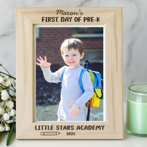 May include: A wooden photo frame with the text "Mason's FIRST DAY OF PRE-K" and "LITTLE STARS ACADEMY 2025". The frame holds a photo of a young child with a backpack. A yellow speech bubble says "CUSTOMIZE: NAME GRADE SCHOOL AND YEAR".