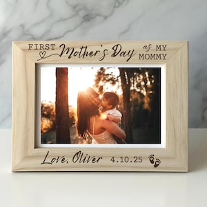 May include: A light-colored wooden picture frame with the text "FIRST Mother's Day as my Mommy" and "Love, Oliver 4.10.25" engraved on it. The frame holds a photo of a mother and child. Two small footprints are at the bottom right.