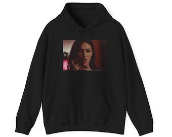 Könnte beinhalten: Ein schwarzer Kapuzenpullover mit einem rechteckigen Grafikdruck auf der Brust. Der Druck zeigt ein fotografisches Bild einer Person mit dunklem Haar, die einen Lutscher im Mund hält, vor einem dunklen, rötlichen Hintergrund.