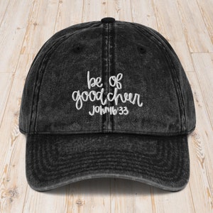 May include: Black distressed denim baseball cap with white embroidered text that reads "be of good cheer John 16:33".