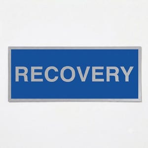 May include: A rectangular sign featuring a solid blue background and a thin silver border. The word RECOVERY is printed in large, bold, silver capital letters across the centre of the sign, creating a clear contrast against the blue surface.
