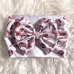May include: White headband with a large, white bow. The bow is covered in a white and brown fabric with a repeating pattern of Harry Potter themed images, including glasses, wands, and a flying car.