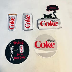 May include: Five different stickers featuring the Diet Coke logo. One sticker shows a skeleton dancing with the text "Dying for a Diet Coke". Another sticker shows a black cat peeking over a can of Diet Coke with the text "Don't Even Think about it."