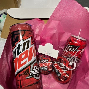 May include: A gift box filled with pink tissue paper and a Mountain Dew Code Red themed gift set. The set includes a tumbler, a can, and two round coasters with the Mountain Dew Code Red logo. The box also includes a small tag that says "Handmade with love".
