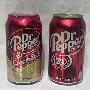 May include: Two red and gold 12-ounce Dr Pepper and Cream Soda cans. The can on the left says "Dr Pepper & Cream Soda" and the can on the right says "Dr Pepper" with the 23 flavors logo.