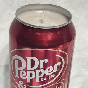 Pu&ograve; includere: Una candela in una lattina di alluminio rossa con una parte superiore di cera bianca e uno stoppino. La lattina ha il testo "Dr Pepper & Cream Soda" e "Est. 1885" stampato su di essa.