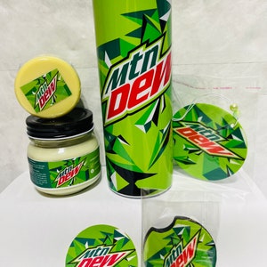 May include: A set of Mountain Dew themed products including a tumbler, candle, car air freshener, and coasters. The tumbler is green with a black and white Mountain Dew logo. The candle is in a glass jar with a white label and the Mountain Dew logo. The car air freshener is a green and white circle with the Mountain Dew logo. The coasters are round and have the Mountain Dew logo.