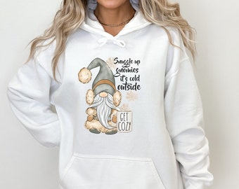 May include: White hoodie with a gray gnome holding a mug that says "Get Cozy". The text on the hoodie says "Snuggle up gnomies it's cold outside".